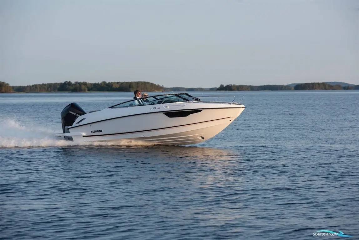 A white Flipper 700 DC boat speeds across a calm lake, with two passengers enjoying the ride against a scenic backdrop.
